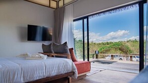 Een slaapkamer met een groot bed, een flatscreen televisie, uitzicht op het groen door een schuifpui en een balkon met een houten terras.