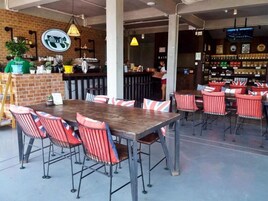 Un área de comedor al aire libre con un muro de ladrillo, una barra y sillas con rayas rojas.