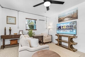 A living room with a sofa, armchair, coffee table, and a TV mounted on a wooden stand. - Poolside Fun, Pickleball & Coastal Adventures Await in Fort Myers - Jefferson Palms 125-3  - Roelens (Fort Myers Beach)
