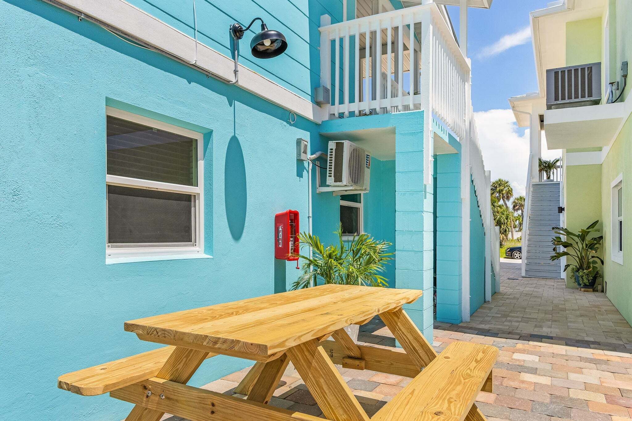 A narrow outdoor corridor with a wooden picnic table and a red mailbox.