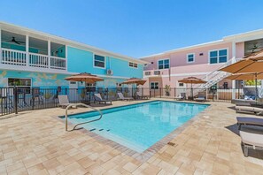 A swimming pool with lounge chairs and umbrellas, surrounded by a building with a mural and a staircase. - Poolside Fun, Pickleball & Coastal Adventures Await in Fort Myers - Jefferson Palms 125-4 - Roelens (Fort Myers Beach)