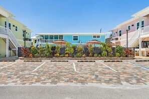 A parking area with a paved surface, a row of umbrellas, and a building with a blue facade in the background. - Poolside Fun, Pickleball & Coastal Adventures Await in Fort Myers - Jefferson Palms 125-4 - Roelens (Fort Myers Beach)