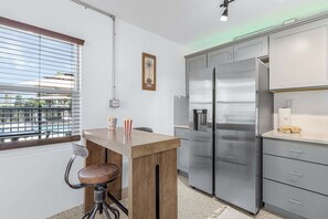 A compact kitchen with a built-in refrigerator, a wooden bar stool, and a window with blinds. - Poolside Fun, Pickleball & Coastal Adventures Await in Fort Myers - Jefferson Palms 125-4 - Roelens (Fort Myers Beach)