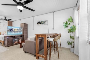 A compact living space with a television, a wooden cabinet, a bar area, and a ceiling fan. - Poolside Fun, Pickleball & Coastal Adventures Await in Fort Myers - Jefferson Palms 125-8 - Roelens (Fort Myers Beach)