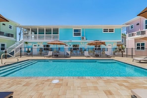 A swimming pool with lounge chairs and umbrellas, surrounded by a building with a mural and a balcony. - Poolside Fun, Pickleball & Coastal Adventures Await in Fort Myers - Jefferson Palms 125-8 - Roelens (Fort Myers Beach)