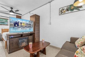 Una sala de estar con televisor mostrando un anuncio de vacaciones, un mueble de madera, un sofá, una mesa de centro y una chimenea.