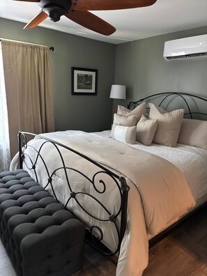 Een slaapkamer met een bed, een plafondventilator, een airconditioningapparaat, een bedlampje en een lijst met een foto aan de muur.