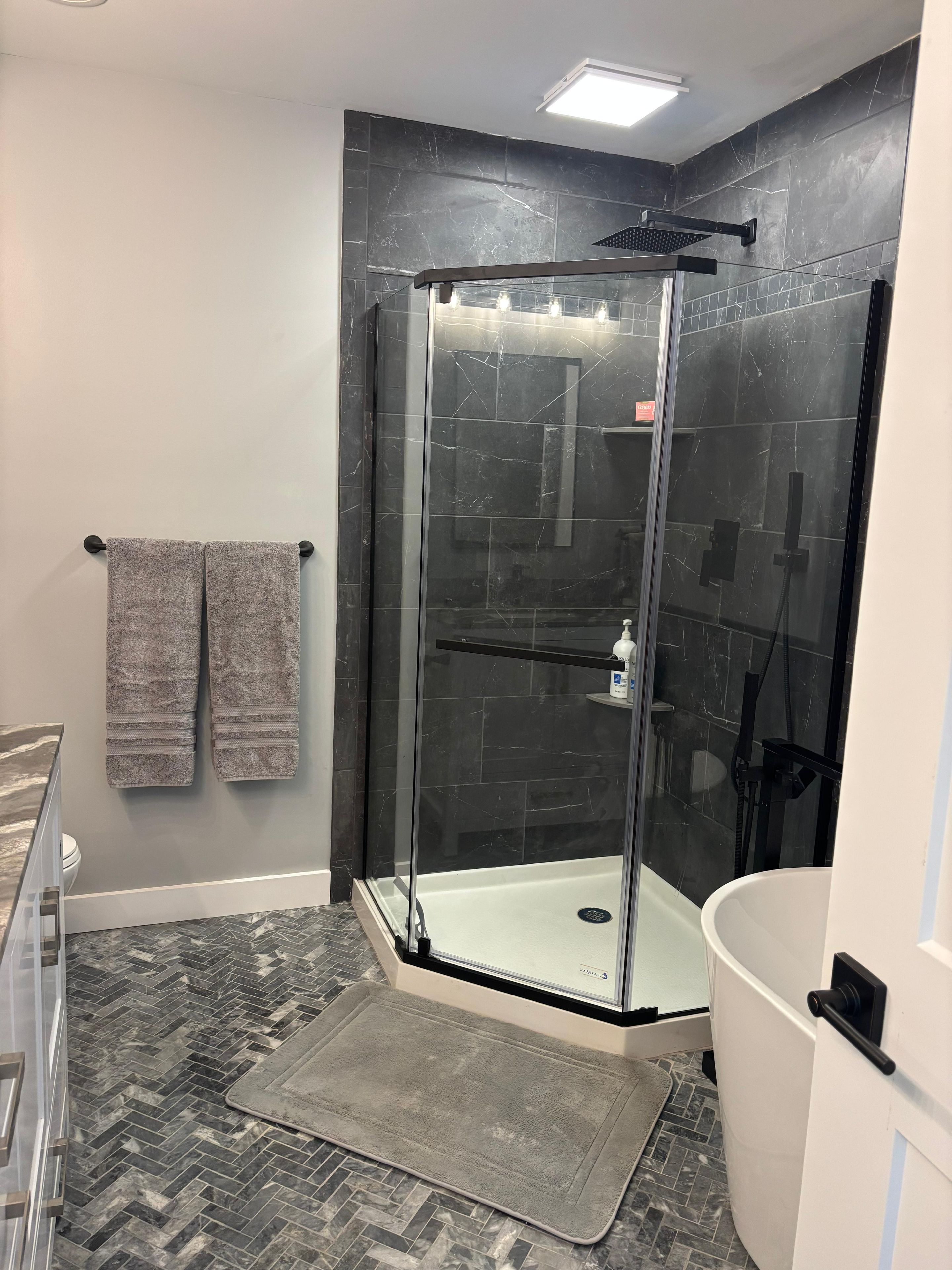 Ein modernes Badezimmer mit einer Duschkabine aus Glas, einer weißen Badewanne und einem Fischgrätenboden.