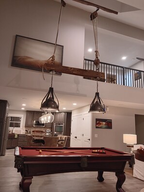 Un grand espace de vie comprenant une table de billard, une table à manger et une cuisine située à l’arrière-plan.