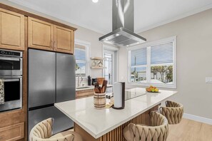 A modern kitchen with stainless steel appliances, a central island with seating, and large windows. - Poolside Fun, Pickleball & Coastal Adventures Await in Fort Myers - Jefferson Palms 127 - Roelens (Fort Myers Beach)