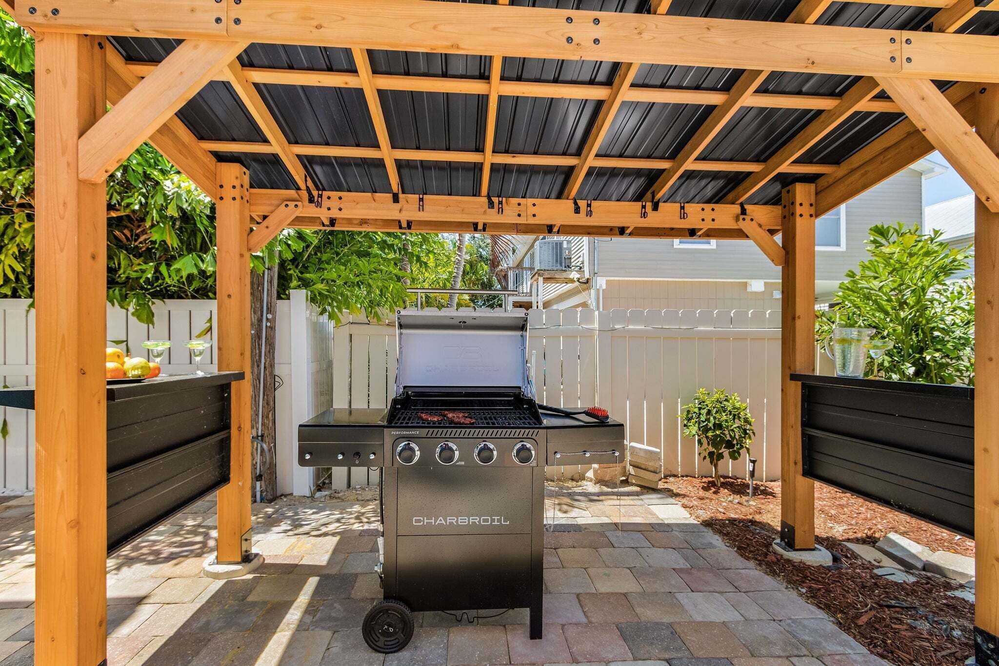 A charcoal grill under a wooden pergola with a brick patio.