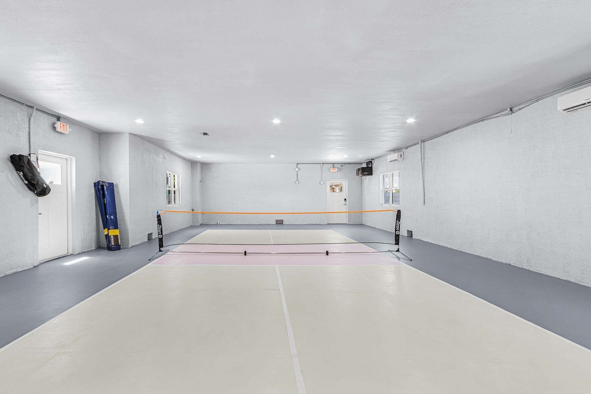 A sports hall with a volleyball net, a door with an exit sign, and a window.