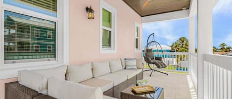 A covered outdoor seating area with a sofa, wicker furniture, a hanging chair, and a ceiling fan.