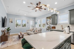 A modern kitchen with a large island, a ceiling fan, and a dining area with a green chair. - Poolside Fun, Pickleball & Coastal Adventures Await in Fort Myers - Jefferson Palms 129 - Roelens (Fort Myers Beach)