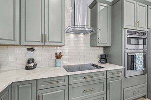 A kitchen with grey cabinets, a white tiled backsplash, a built-in oven, and a coffee maker. - Poolside Fun, Pickleball & Coastal Adventures Await in Fort Myers - Jefferson Palms 129 - Roelens (Fort Myers Beach)