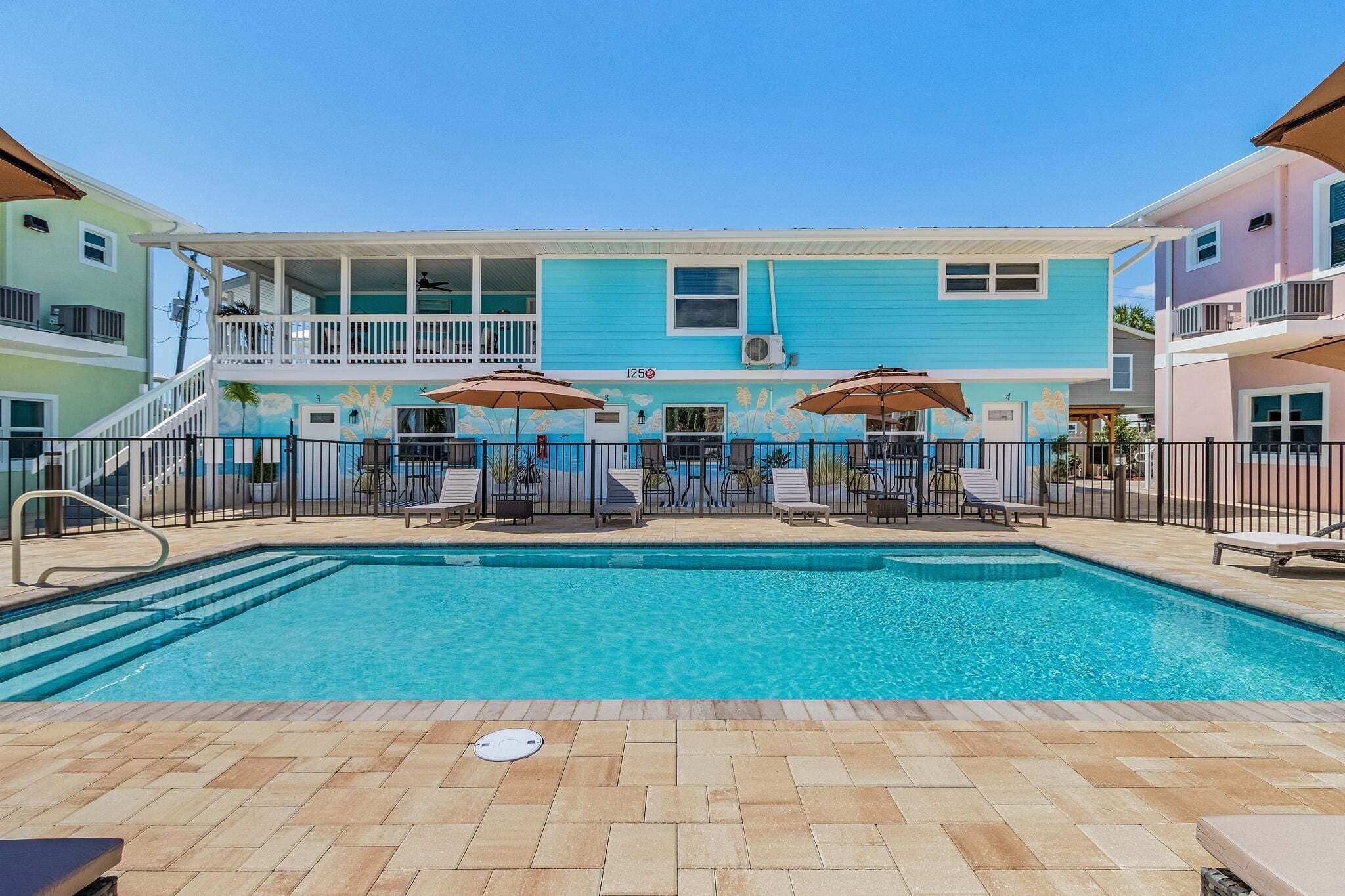 A swimming pool with lounge chairs and umbrellas, surrounded by a building with a mural and a balcony.