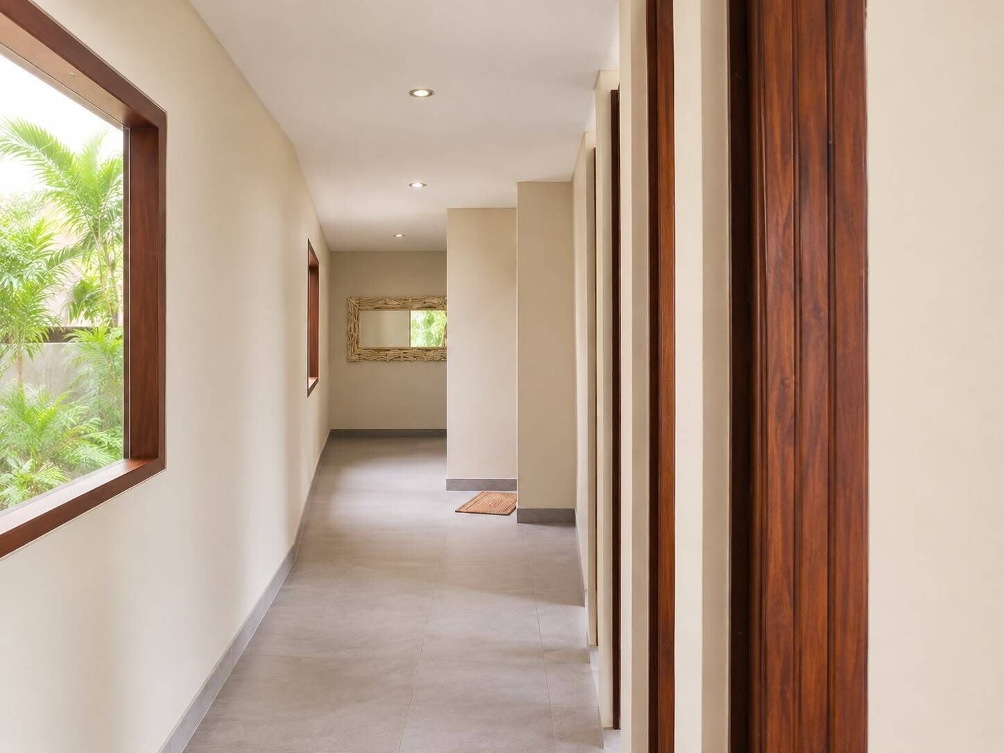 Un pasillo con una puerta de madera, un espejo y una ventana con vistas al verdor.