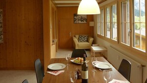 Uma sala de jantar com mesa de madeira posta para dois, uma garrafa de vinho e um quadro na parede.