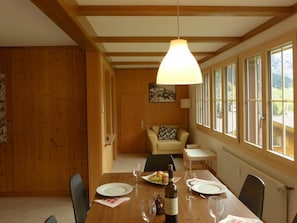 A dining area with a wooden table set for two, a bottle of wine, and a painting on the wall. - Lucie 4-Zimmerwohnung by Interhome (Adelboden)