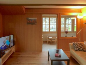 A living room with wooden walls, a television, a table, and a sofa. There is a painting on the wall and a window with a view of the outdoors. - Lucie 4-Zimmerwohnung by Interhome (Adelboden)