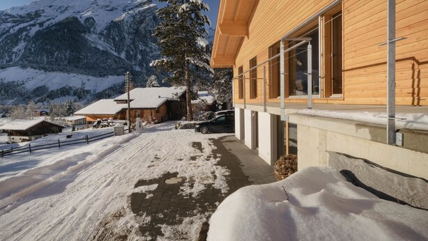 A wooden building with large windows, a snow-covered ground, and mountains in the background. - Chalet Bärgfride Appartement/Fewo, Dusche, WC, 1 Schlafraum 3-Zimmerwohnung by Interhome (Kandersteg)