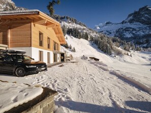 A wooden chalet with a car parked in front, surrounded by snow-covered mountains. - Chalet Bärgfride Appartement/Fewo, Dusche, WC, 1 Schlafraum 3-Zimmerwohnung by Interhome (Kandersteg)