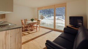 A modern living space with a kitchen, dining area, and a large sliding glass door leading to a snowy outdoor area. - Chalet Bärgfride Appartement/Fewo, Dusche, WC, 1 Schlafraum 3-Zimmerwohnung by Interhome (Kandersteg)