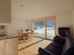 A modern living space with a kitchen, dining area, and a large sliding glass door leading to a snowy outdoor area. - Chalet Bärgfride Appartement/Fewo, Dusche, WC, 1 Schlafraum 3-Zimmerwohnung by Interhome (Kandersteg)