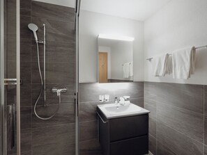 A modern bathroom with a glass shower enclosure, a sink with a mirror, and a towel rack. - Chalet Bärgfride Appartement/Fewo, Dusche, WC, 1 Schlafraum 3-Zimmerwohnung by Interhome (Kandersteg)