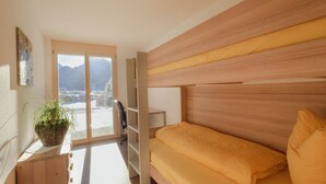 A room with a bed, a desk, a chair, a potted plant, and a view of mountains through a large window. - Chalet Bärgfride Appartement/Fewo, Dusche, WC, 1 Schlafraum 3-Zimmerwohnung by Interhome (Kandersteg)
