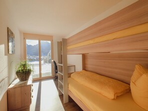 A room with a bed, a desk, a chair, a potted plant, and a view of mountains through a large window. - Chalet Bärgfride Appartement/Fewo, Dusche, WC, 1 Schlafraum 3-Zimmerwohnung by Interhome (Kandersteg)
