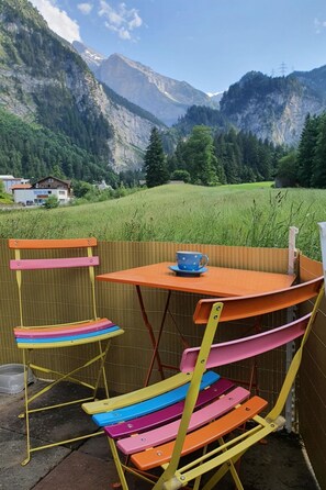 A colorful outdoor seating area with a table and chairs, overlooking a mountainous landscape. - Schwendli Appartement/Fewo, Dusche, WC 3-Zimmerwohnung by Interhome (Kandersteg)
