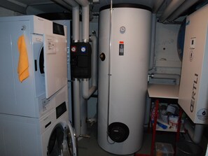 A room with a large cylindrical water heater, a washing machine, and a shelf with various items. - Hubelhüsi Appartement/Fewo, Dusche oder Bad, WC, 4 oder mehr Schlafräume by Interhome (Adelboden)