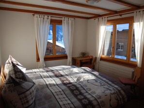 Ett sovrum med en säng, ett litet bord, en stol och ett fönster med utsikt över ett snötäckt landskap.