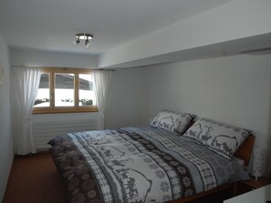 Ein Schlafzimmer mit einem Bett, einem Fenster mit Vorhängen und einer Deckenleuchte.