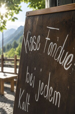 A chalkboard with the text 'Masse Fondue bei jedem Kalt' written on it, set against a backdrop of a wooden fence and mountains. - Schermtanne Appartement/Fewo, Bad, WC, 1 Schlafraum Wohnung Nr 4 by Interhome (Adelboden)