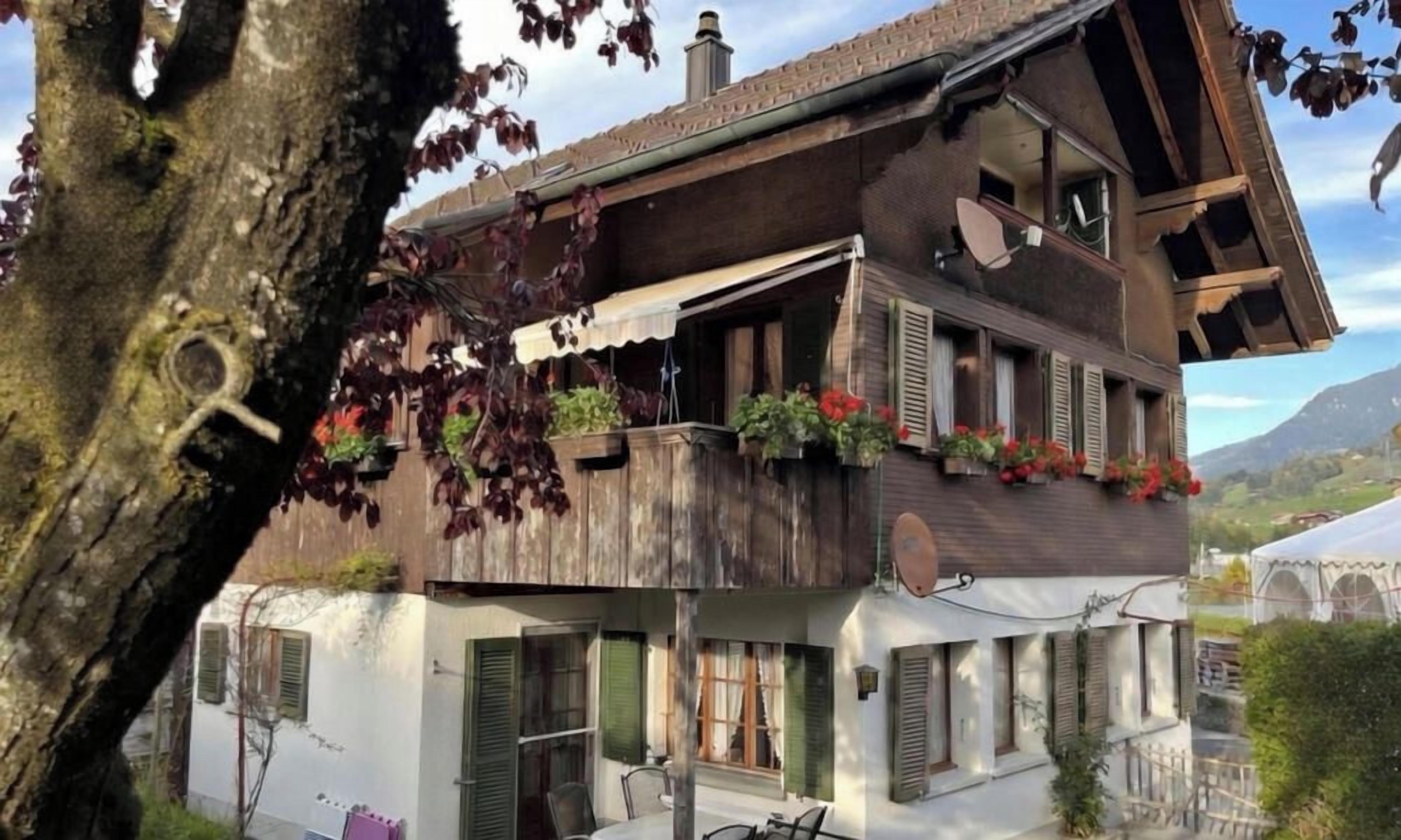 Un bâtiment à deux étages doté d’un balcon, de fenêtres avec volets et d’un arbre au premier plan.