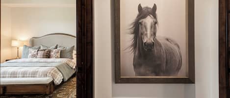 Un dormitorio con cama, almohadas, una mesita de noche, una lámpara y un cuadro enmarcado con un caballo en la pared.