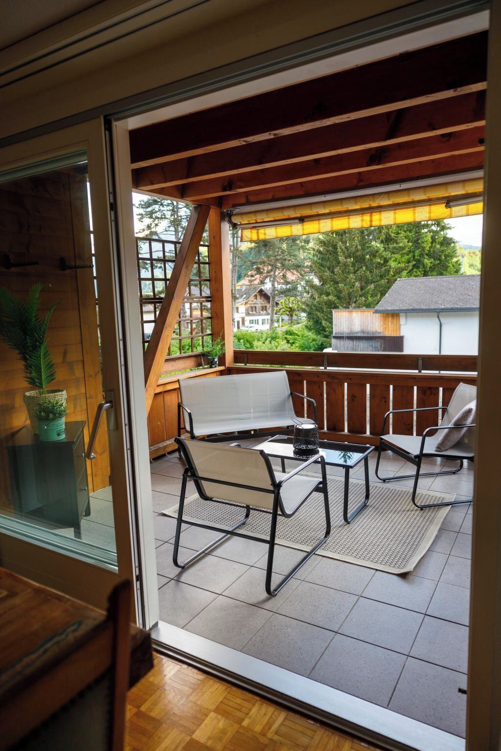 An outdoor patio with a glass door leading to a wooden deck, furnished with a table and two chairs.