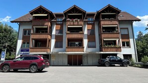 Un edificio de varios pisos con balcones de madera, un letrero que indica un centro de salud y dos automóviles estacionados.