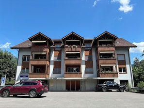 A multi-story building with wooden balconies, a sign for a health center, and two parked cars. - Mountain View Appartement/Fewo, Dusche, WC, 3 Schlafräume 4.5 Zimmer-Wohnung by Interhome (Frutigen)