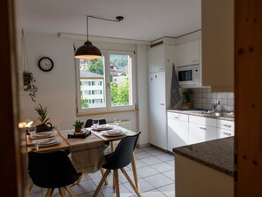 A modern kitchen with white cabinets, a microwave, and a dining area with a table set for two. - Mountain View Appartement/Fewo, Dusche, WC, 3 Schlafräume 4.5 Zimmer-Wohnung by Interhome (Frutigen)