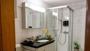 Un baño moderno con ducha envuelta en vidrio, lavamanos con espejo superior y retrete.