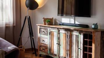 Une pièce avec un plancher en bois, un téléviseur fixé au mur, une lampe et un meuble avec des tiroirs.