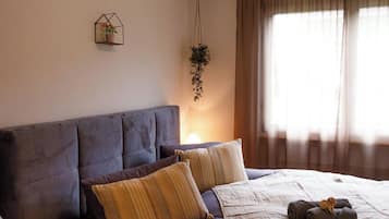 Une chambre à coucher avec un lit, une table de chevet, une plante suspendue et une fenêtre avec des rideaux.