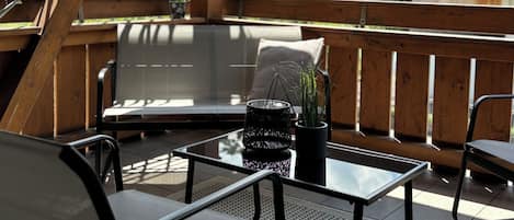 A wooden deck with a glass table, a bench, and a potted plant.
