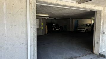Un parking souterrain aux murs en béton, avec quelques voitures garées et une porte de sortie bien visible.