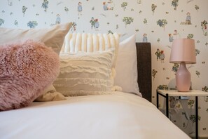 A bedroom with a bed, pillows, a bedside table with a lamp, and a wall with a floral pattern. - Oxfordshire home Surrounded by Greenery (Bessels Leigh)