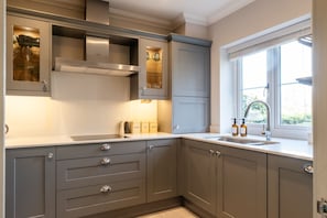 A modern kitchen with grey cabinets, a stainless steel range hood, and a window with a view of greenery.