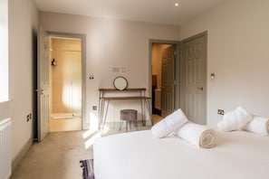 A hotel room with a bed, a bedside table, a mirror, and a door leading to a bathroom.